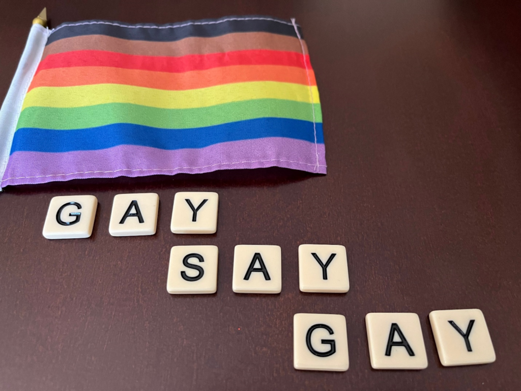Pride flag and tiles on a table that spell out "Gay Say Gay"