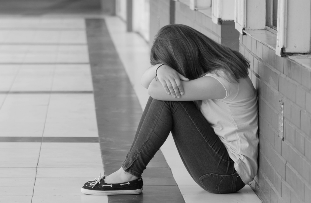 Girl sitting in school hallway with head on crossed arms.